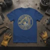 Heemeyer Welding and Demolition Granby Colorado circular logo on a blue t-shirt, featuring an excavator and welding graphics