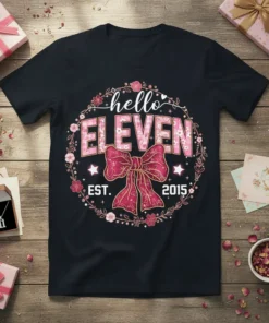 Black t-shirt with "hello ELEVEN EST. 2015" in pink floral design, featuring a bow and wreath