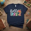 Hello Pre-K text with colorful alphabet letters, an apple, and school supplies graphic on a navy t-shirt