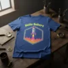 Blue t-shirt with "Hello Robert" text and a colorful rocket ship launching within a hexagon frame