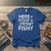 Here Fishy Fishy Fishy text with fish and fishing lure graphic on blue t-shirt