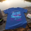 Blue t-shirt with "HERE FISHY FISHY FISHY" in neon colors, fishing rod, and fish graphics