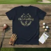 He's Golfing t-shirt design with crossed golf clubs and a golfer graphic in a laurel wreath