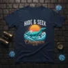 Hide & Seek Champion Since 1933 t-shirt featuring a blue plesiosaur swimming through waves with a sunset background