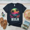 Hilo Hawaii text with tropical sunset, palm trees, and hibiscus flowers graphic on a navy t-shirt