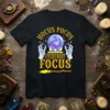 Hocus Pocus Everybody Focus text with crystal ball and witch hands graphic on a black t-shirt