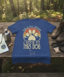 Hold My Drink I Gotta Pet This Dog quote on a blue t-shirt with paw print and mountain graphic