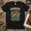 Hookin' Ain't Easy fishing t-shirt design with a bass jumping out of water and crossed fishing rods