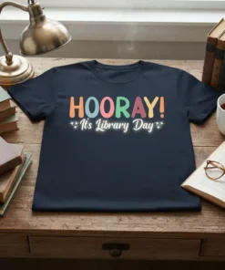 HOORAY! It's Library Day text design in colorful block letters with small star accents on a navy blue t-shirt
