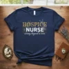 Navy t-shirt with gold and white text reading "HOSPICE NURSE caring beyond a cure" surrounded by floral elements