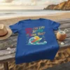 Blue t-shirt with colorful text "How Can Life Get Better Than This?" above a surf wave, surfboard, palm trees, and