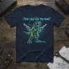 How You Like Me Now? text above a green robotic T-Rex holding two guns, on a navy t-shirt