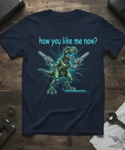 How You Like Me Now? text above a green robotic T-Rex holding two guns, on a navy t-shirt