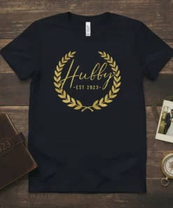 Hubby -EST 2023- text inside a gold laurel wreath on a black t-shirt, commemorating a new marriage