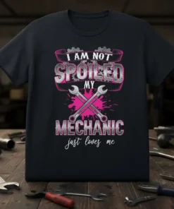 I AM NOT SPOILED MY MECHANIC just loves me text with crossed wrenches and pink paint splatters on a black
