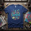 Blue t-shirt with the text "I arted" in vibrant, colorful, cartoon-style lettering, surrounded by art supplies like paintbrushes and a