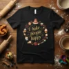 Black t-shirt with "I bake people happy" quote surrounded by a wreath of cupcakes, cake, and berries