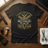Black t-shirt with gold text: "I Can't Fix Stupid But I Can Fix Your Hair" and barber graphics