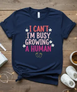 Navy blue t-shirt with "I Can't I'm Busy Growing A Human" text in pink and red, decorated with small white
