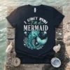 I Can't Run I'm A Mermaid text with a teal mermaid tail and jellyfish graphic on a black t-shirt