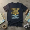 Navy t-shirt with yellow text "I COULD USE A GOOD PADDLING" above a graphic of a kayaker on water with