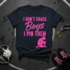 Pink text "I DON'T CHASE Boys I PIN THEM" with a female wrestler graphic on a dark navy t-shirt