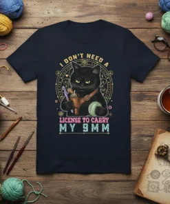Black cat with knitting supplies and text "I DON'T NEED A LICENSE TO CARRY MY 9MM" on a navy t-shirt