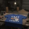 T-shirt with "I Eat Cement" text and a muscular cat character holding a bag of cement mix