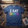 I Eat Crayons text design with dripping rainbow colors on a navy t-shirt, surrounded by art supplies