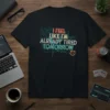 I FEEL LIKE I'M ALREADY TIRED TOMORROW quote in distressed, colorful typography on a black t-shirt, with subtle tech graphics
