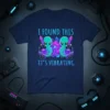 T-shirt design with text "I FOUND THIS IT'S VIBRATING," featuring two cute aliens holding black cats with planets and crystals