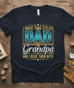 I Have Two Titles Dad & Grandpa And I Rock Them Both quote on a navy t-shirt, featuring bold blue