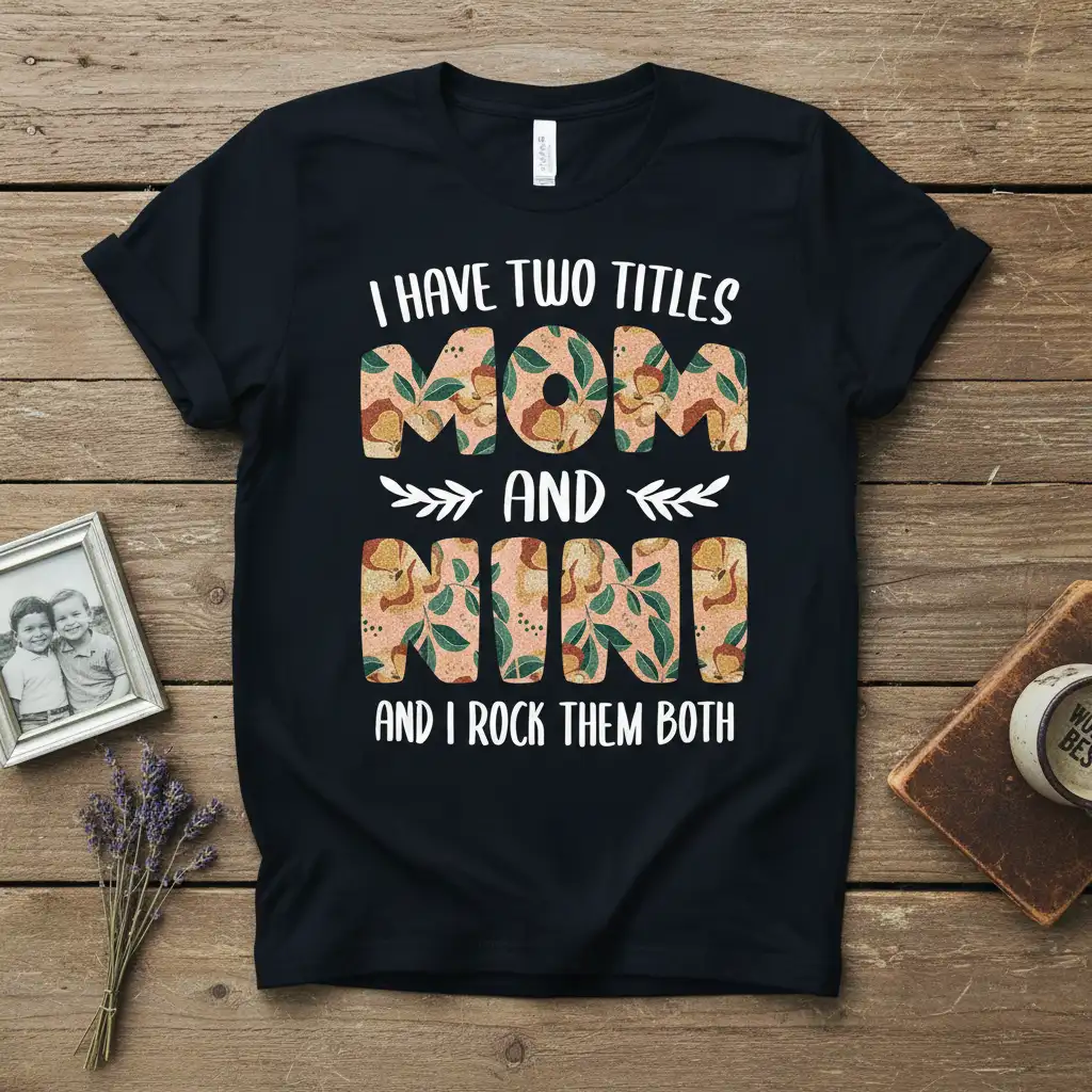 I Have Two Titles Mom and Nini quote design with decorative letters and leaf accents on a black tee