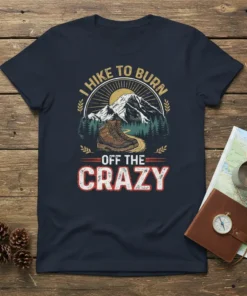 I Hike To Burn Off The Crazy quote on a dark navy t-shirt with a hiking boot, mountains, and sun