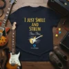 Navy t-shirt with gold text "I JUST SMILE AND STRUM Steve Stine" and a graphic of a golden electric guitar