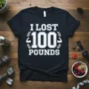 I LOST 100 POUNDS text with muscle graphics on a navy t-shirt, celebrating weight loss achievement
