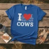 I LOVE COWS t-shirt design with white text, a red heart, two cows, and farm buildings