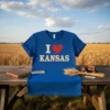 Blue t-shirt with "I Love Kansas" text and a red heart graphic, featuring a wheat field background