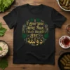 Black t-shirt with gold text "I Love You More Than Iraqis Love Dolma" and Arabic script, framed by green leaves