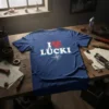 Blue t-shirt with white text "I LÜCKI" and a red heart graphic above. Includes a compass rose illustration below