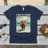 I May Be Stupid Highland Cow T-Shirt with a fuzzy cow standing on a beach with waves