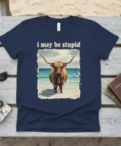 I May Be Stupid Highland Cow T-Shirt with a fuzzy cow standing on a beach with waves