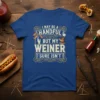 I May Be A Handful But My Weiner Sure Isn't text with hot dog graphics on a blue t-shirt