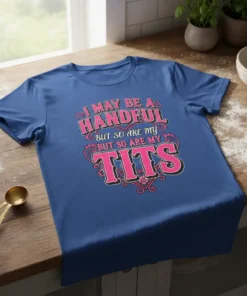 I May Be A Handful But So Are My Tits quote on a blue t-shirt, featuring pink and black lettering