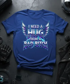 I Need a Hug From a Bad Bitch bold text design with wings and lightning graphics on a blue t-shirt