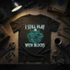 I Still Play With Blocks text with a blueprint-style V8 engine graphic on a black t-shirt