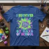 I SURVIVED 67 DAYS OF SCHOOL text with a colorful explosion graphic featuring school supplies on a blue t-shirt