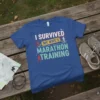 Blue t-shirt with the text "I SURVIVED MY WIFE'S MARATHON TRAINING" in white and teal, featuring running graphics