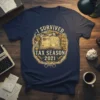 I SURVIVED TAX SEASON 2021 text with an open book graphic and tax-related icons on a navy t-shirt
