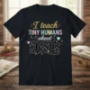 Christian t-shirt with "I teach TINY HUMANS about Jesus" in colorful glitter and script fonts, featuring small stick figures and